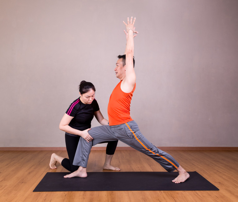 teacher of yoga for sport assisting a student with a yoga pose